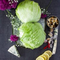 two pieces of iceberg lettuce on a wooden board and some lemon slices around it with a wedge of blue cheese