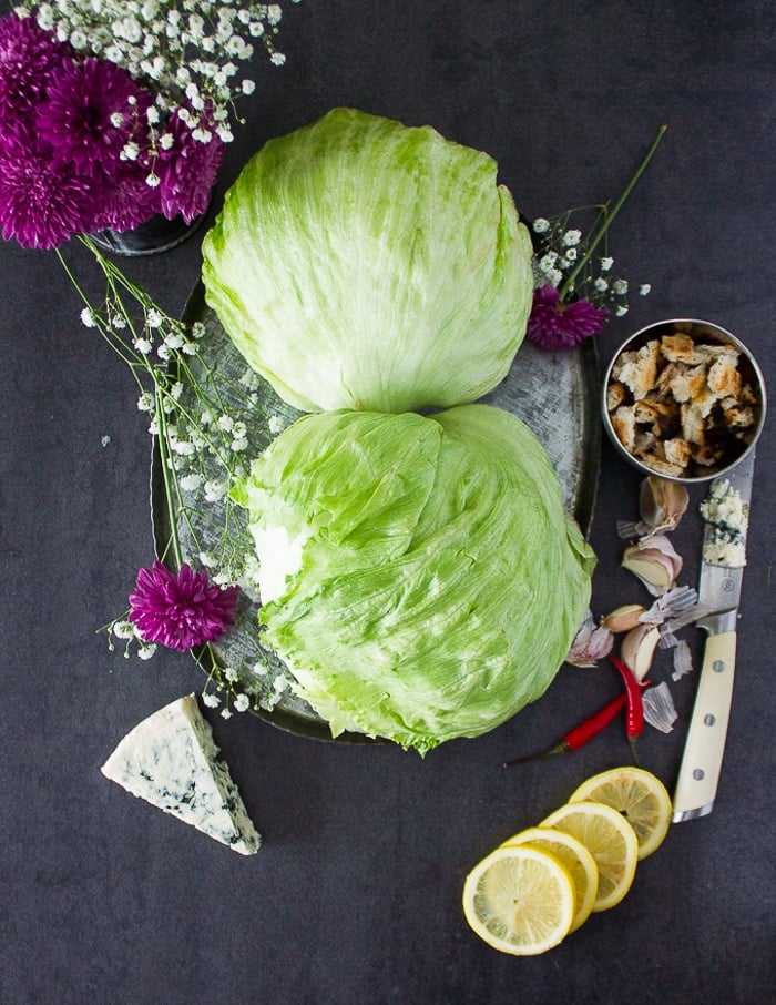 two pieces of iceberg lettuce on a wooden board and some lemon slices around it with a wedge of blue cheese