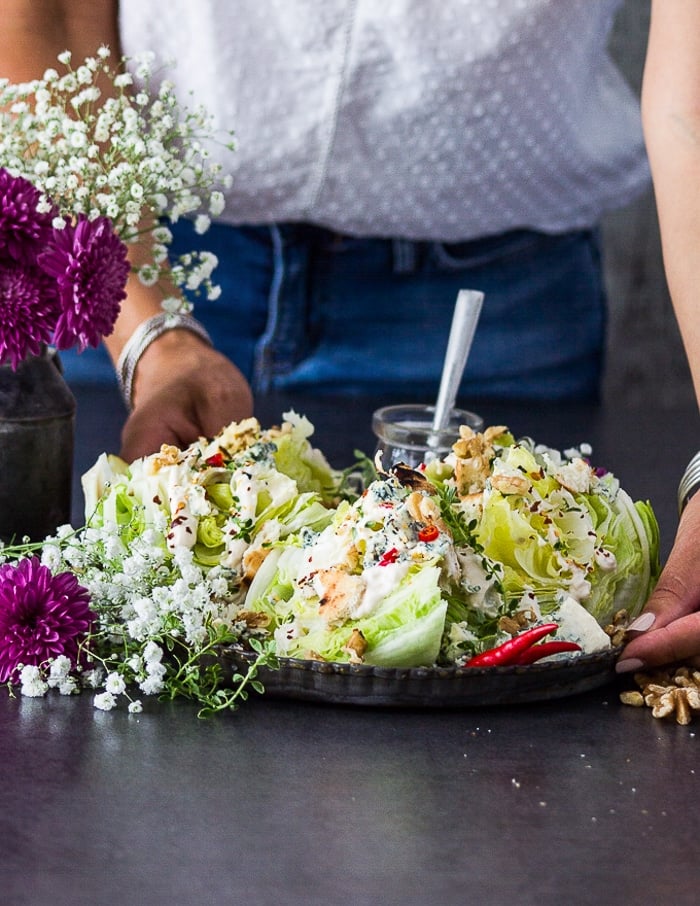 A hand holding a tray of wedge4 salad all dressed u p and topped with all the toppings ready to serve