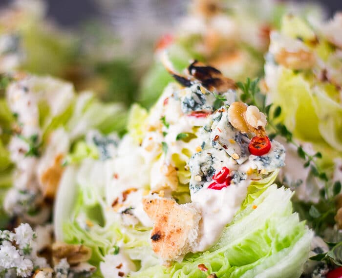close up of a wedge salad dressed in blue cheese dressing and topped with croutons, chillies and seasoning