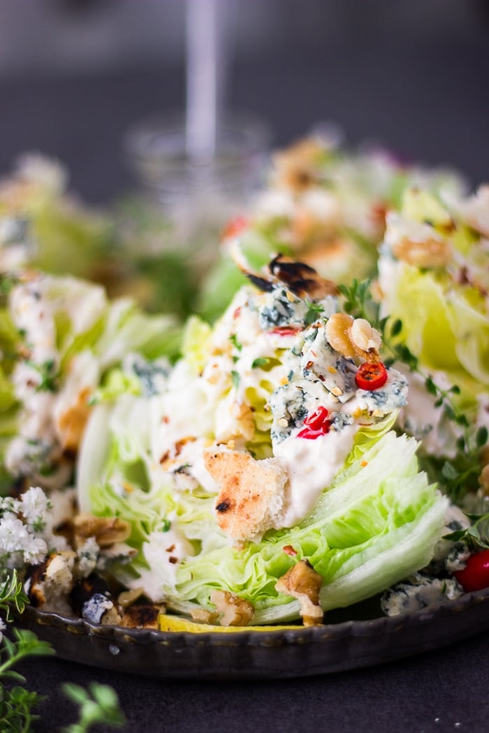 close up of a wedge salad dressed in blue cheese dressing and topped with croutons, chillies and seasoning