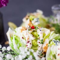 side view close up of one wedge salad showing the blue cheese dressing drizzled over the wedge and showing the toppings