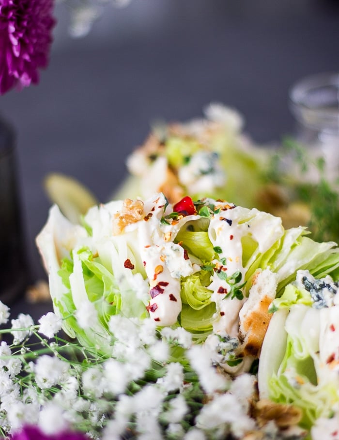 side view close up of one wedge salad showing the blue cheese dressing drizzled over the wedge and showing the toppings