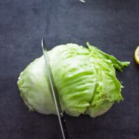 A hand cutting the ice berg lettuce using a serrated knife into thirds to make wedges