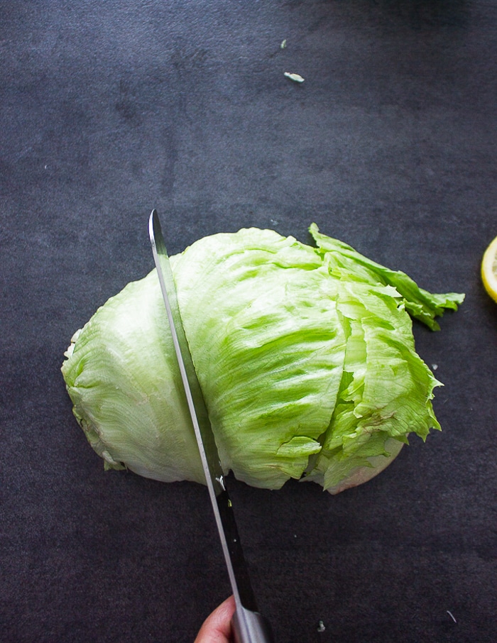 A hand cutting the ice berg lettuce using a serrated knife into thirds to make wedges