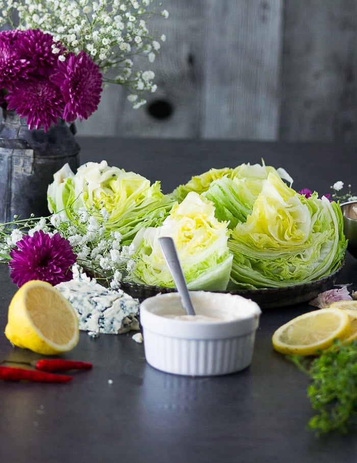 A bowl of blue cheese dressing placed next to cut up iceberg wedges 