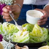 A hand drizzling the blue cheese dressing over the ice berg lettuce wedge