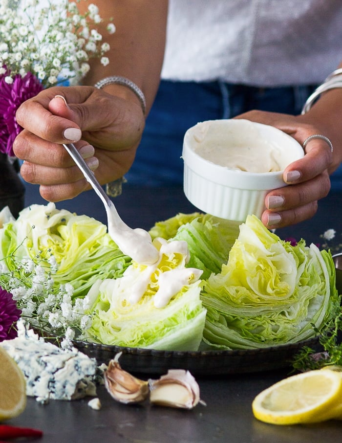 A hand drizzling the blue cheese dressing over the ice berg lettuce wedge