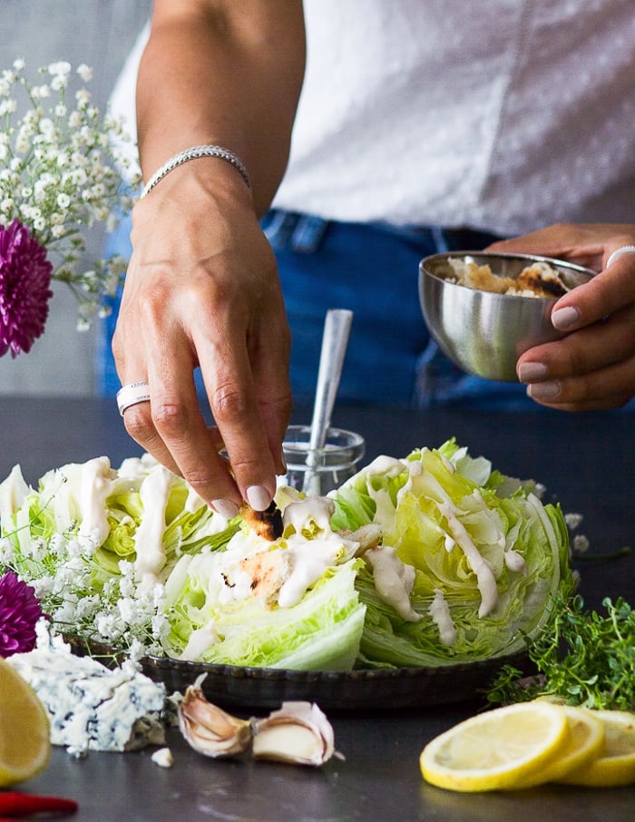 A hand adding in the croutons over the wedge salad dressed with blue cheese dressing