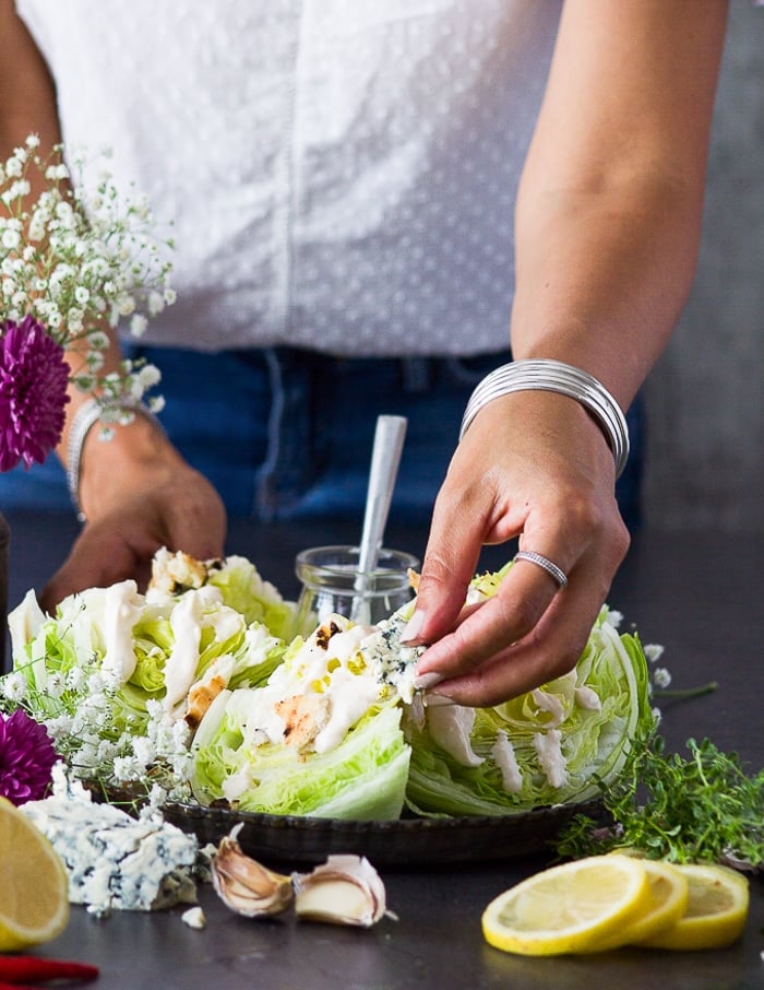 A hand adding crumbles of blue cheese over the wedge salad 