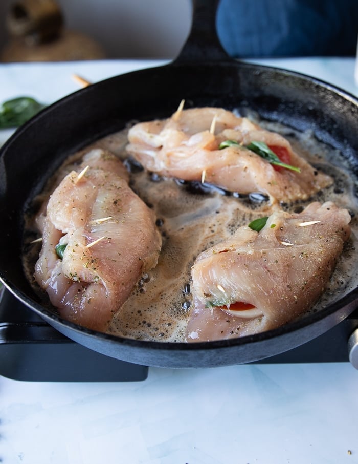 caprese chicken searing in a hot skillet with butter, top side down