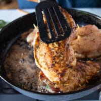 A tong flipping one side of the caprese chicken to show the golden crust