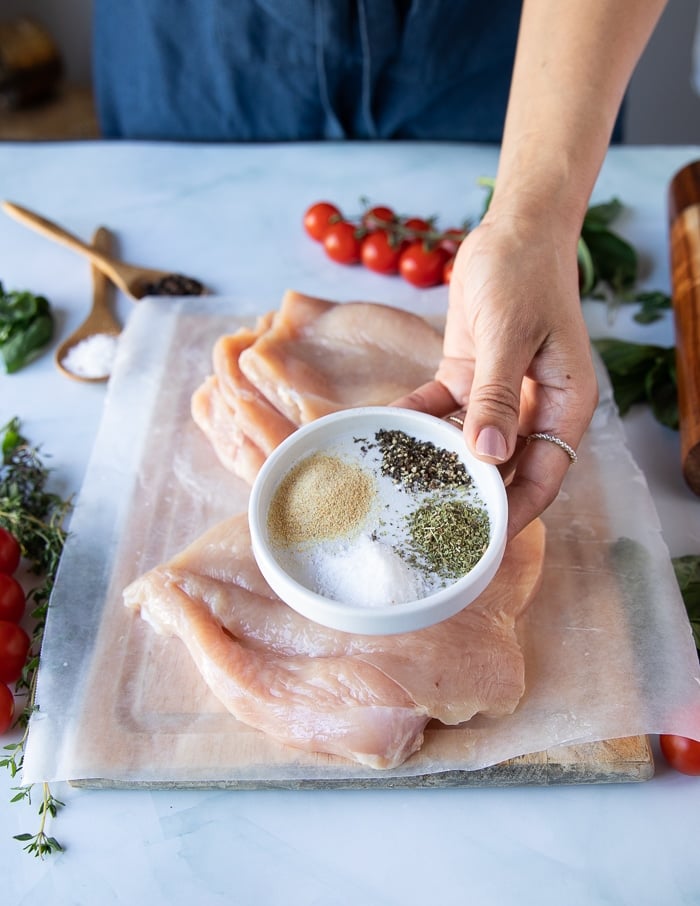 a hand holding a bowl of chicken seasoning to sprinkle on the inside and outside of the chicken 