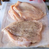 butterflied chicken breasts on a wooden board lined with paper that are seasoned on both sides