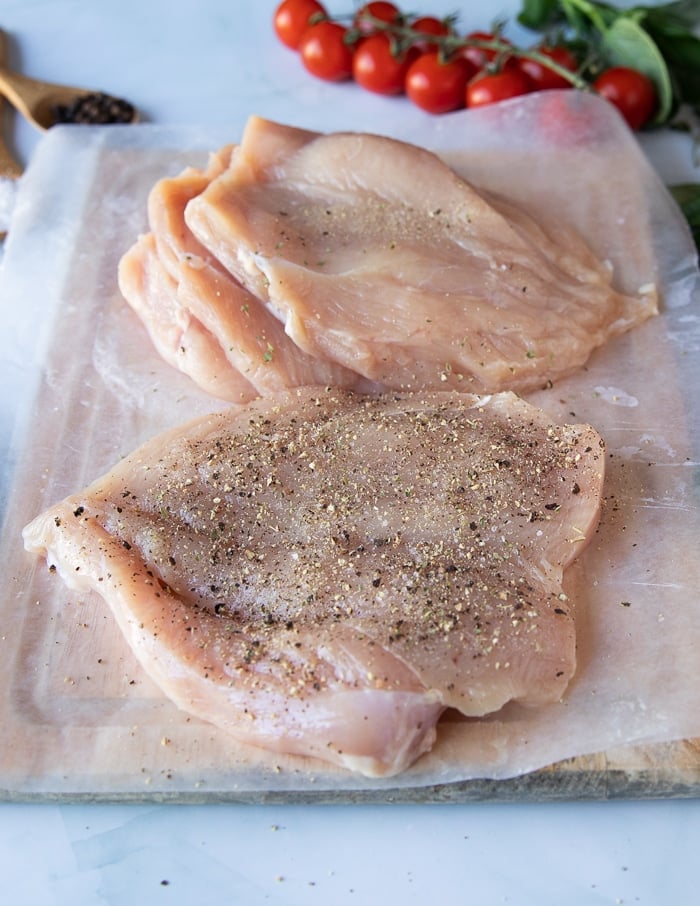 butterflied chicken breasts on a wooden board lined with paper that are seasoned on both sides