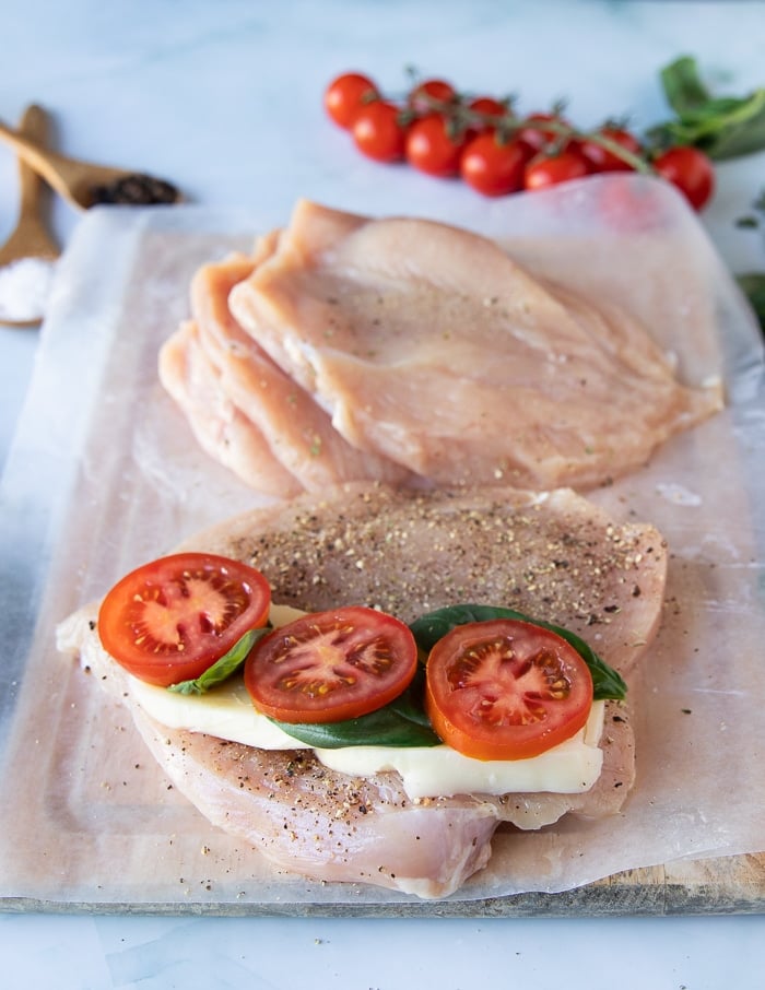 A chicken breast with layers of mozzarella cheese, tomatoes and lots of fresh basil leaves on top