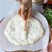 Spreading white sauce on the pizza crust.