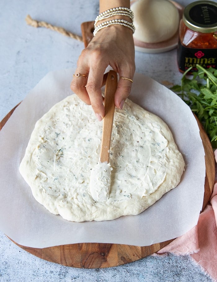 Spreading white sauce on the pizza crust.