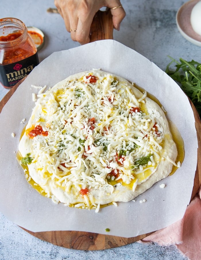 Uncooked pizza ready for the oven covered in mozzarella and drizzled with harissa sauce.