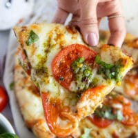 Close-up of one slice of Caprese Pizza held by female hand.