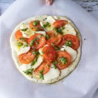 Layered mozzarella and tomatoes on an uncooked pizza crust with basil pesto added.