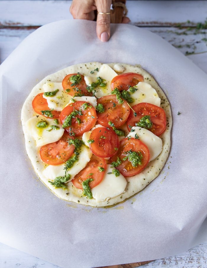 Layered mozzarella and tomatoes on an uncooked pizza crust with basil pesto added.