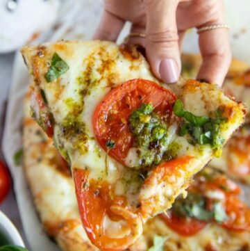 Close-up of one slice of Caprese Pizza held by female hand.