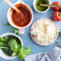 Ingredients for air fryer pizza including pizza sauce, basil pesto, fresh basil, mozzarella cheese and pizza dough