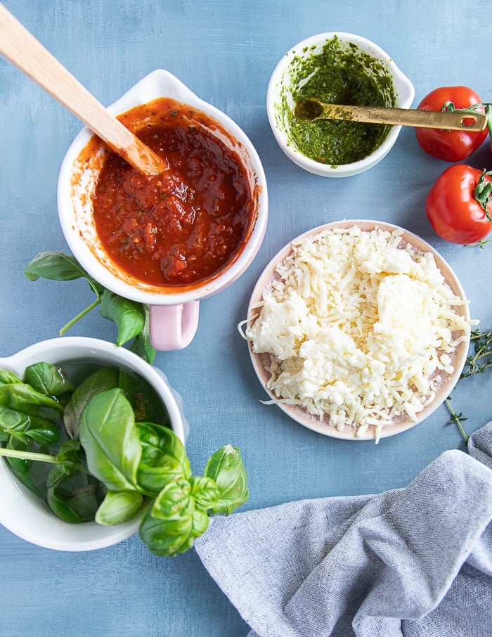Ingredients for air fryer pizza including pizza sauce, basil pesto, fresh basil, mozzarella cheese and pizza dough
