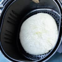 a raw pizza dough at the bottom of an air fryer basket