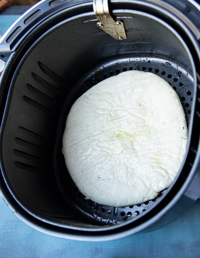 a raw pizza dough at the bottom of an air fryer basket