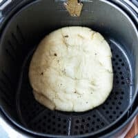 The pizza dough in the air fryer basket after air frying for just a few minutes and ready for the toppings