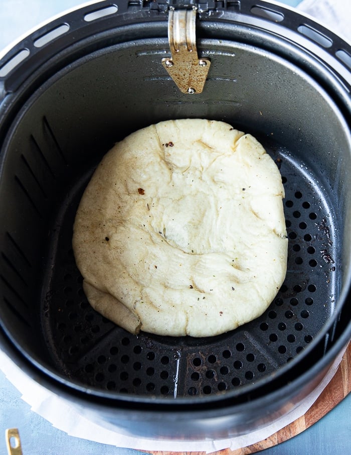 The pizza dough in the air fryer basket after air frying for just a few minutes and ready for the toppings