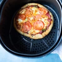 air fryer pizza ready in an air fryer basket with the cheese melted and the crust golden and crisp