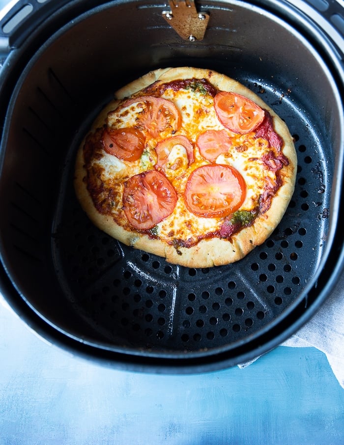 air fryer pizza ready in an air fryer basket with the cheese melted and the crust golden and crisp