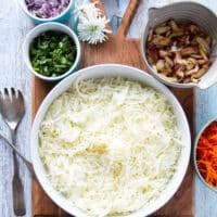 Ingredients for fish taco slaw including cabbage shredded in a bowl, carrots shredded in another bowl, cilantro, diced onions, and shredded apples