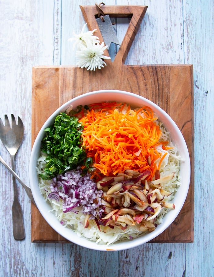 All fish taco slaw recipe ingredients in a large bowl added together: cabbage, carrots, cilantro, onions, apples 