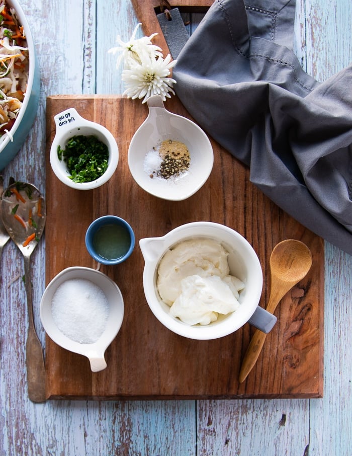 ingredients for coleslaw dressing including a bowl of mayo or sour cream, cilantro, onions, seasoning, sugar and lime juice