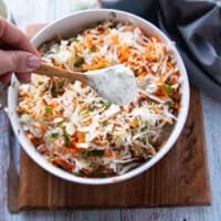 a hand pouring in the coleslaw dressing over the coleslaw