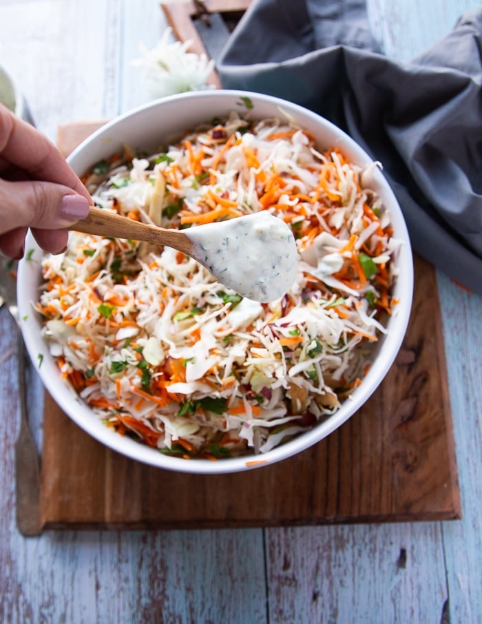 a hand pouring in the coleslaw dressing over the coleslaw