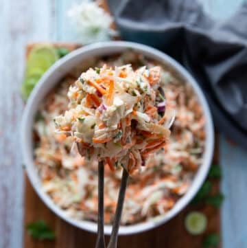 two spoons holding and serving some fish taco slaw showing the texture and coleslaw mixed in