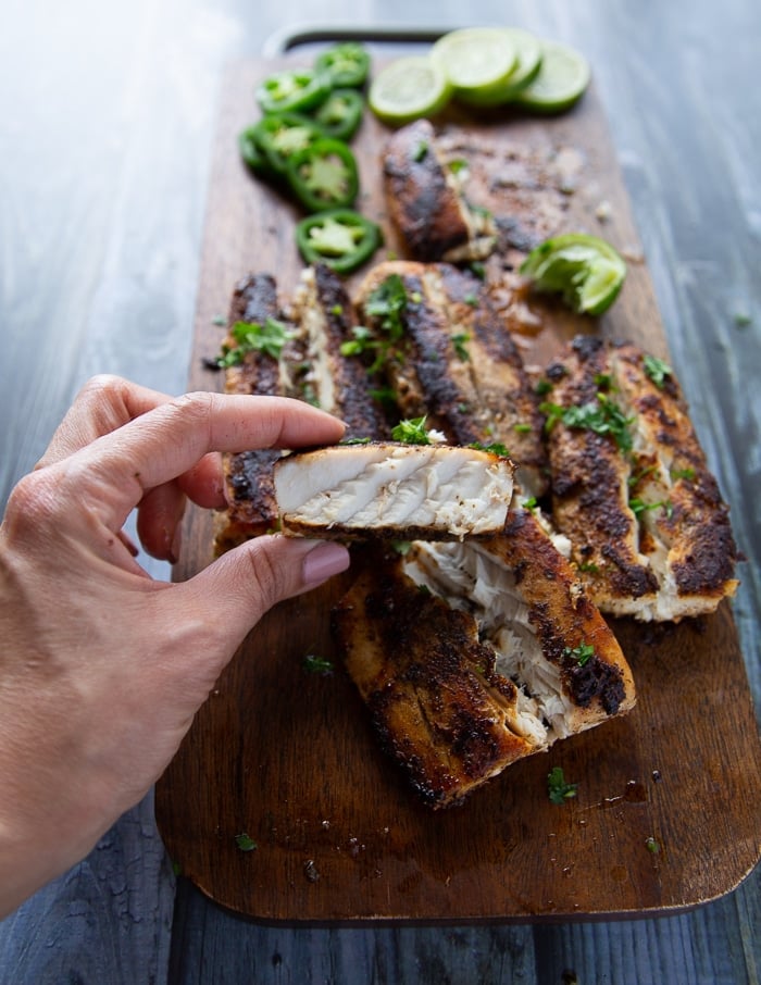 A hand holding a cooked piece of mahi mahi fish to show how thick and firm the texture is