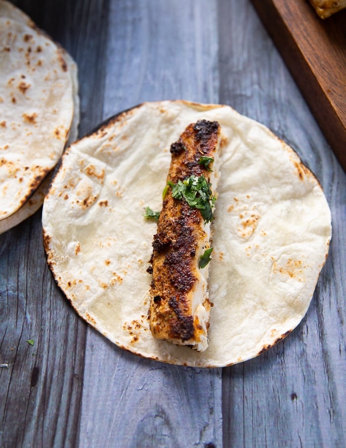 Assembling the mahi mahi tacos with a tortilla and a piece of mahi mahi fish ontop