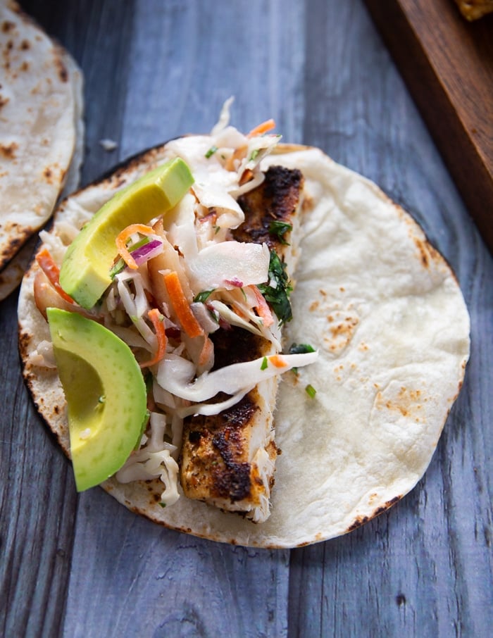 Assembling the mahi mahi tacos with fish slaw added over the fish and avocado slices