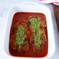 a spread of basil pesto over the layered veal cutlets in tomato sauce