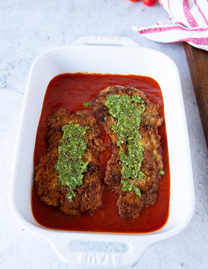 a spread of basil pesto over the layered veal cutlets in tomato sauce