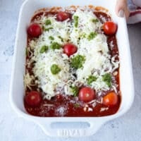 veal parmesan ready to go into the oven: layered veal scallopini over tomato sauce topped with some marinara, basil pesto, mozzarella cheese, parmesan cheese and fresh cherry tomatoes