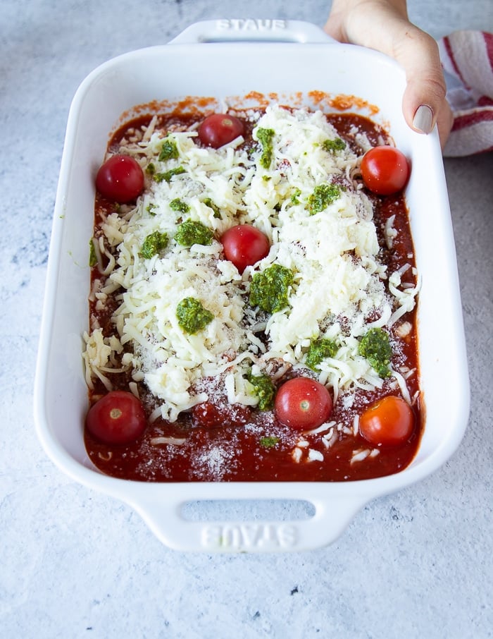 veal parmesan ready to go into the oven: layered veal scallopini over tomato sauce topped with some marinara, basil pesto, mozzarella cheese, parmesan cheese and fresh cherry tomatoes