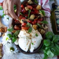 A hand holding a chunk of burrata salad with tomatoes and basil caprese