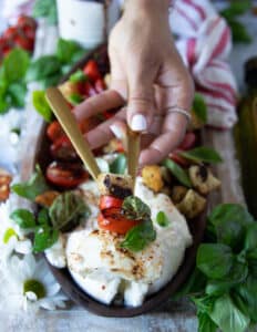 A hand holding a chunk of burrata salad with tomatoes and basil caprese